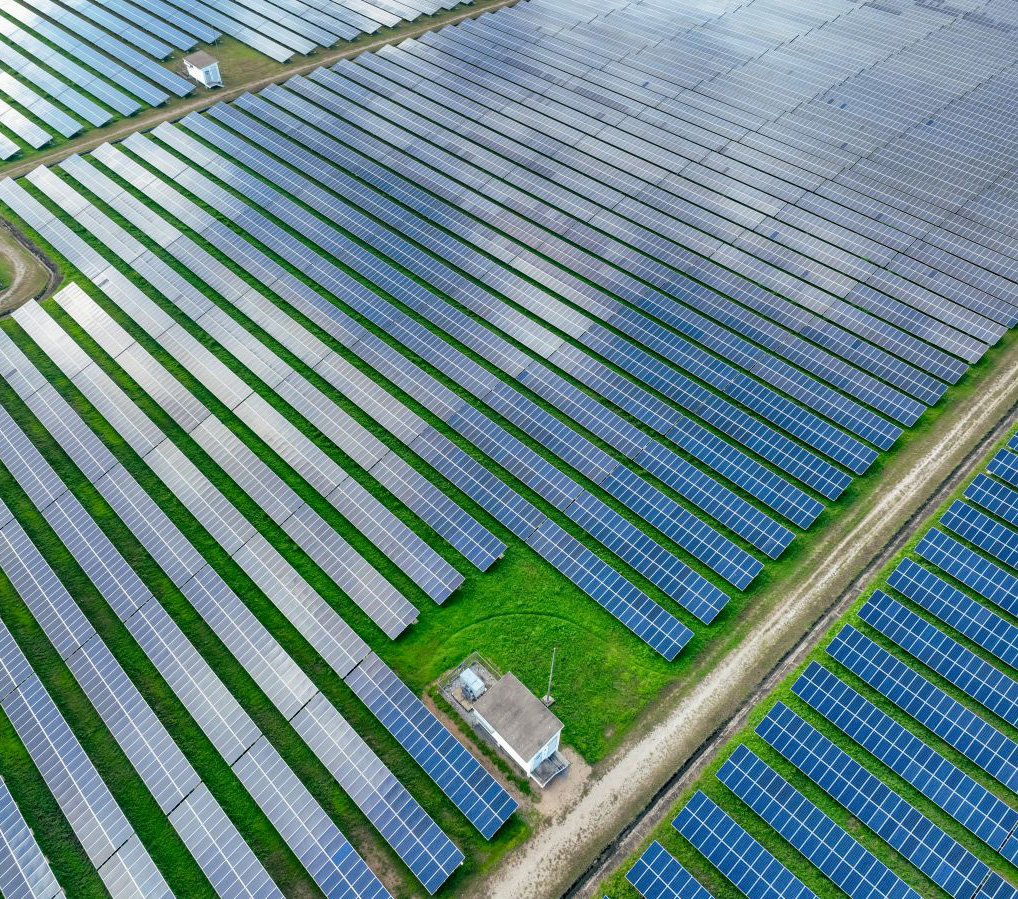 Aerial view of a large solar panel farm with rows of blue panels and a small building in the center.