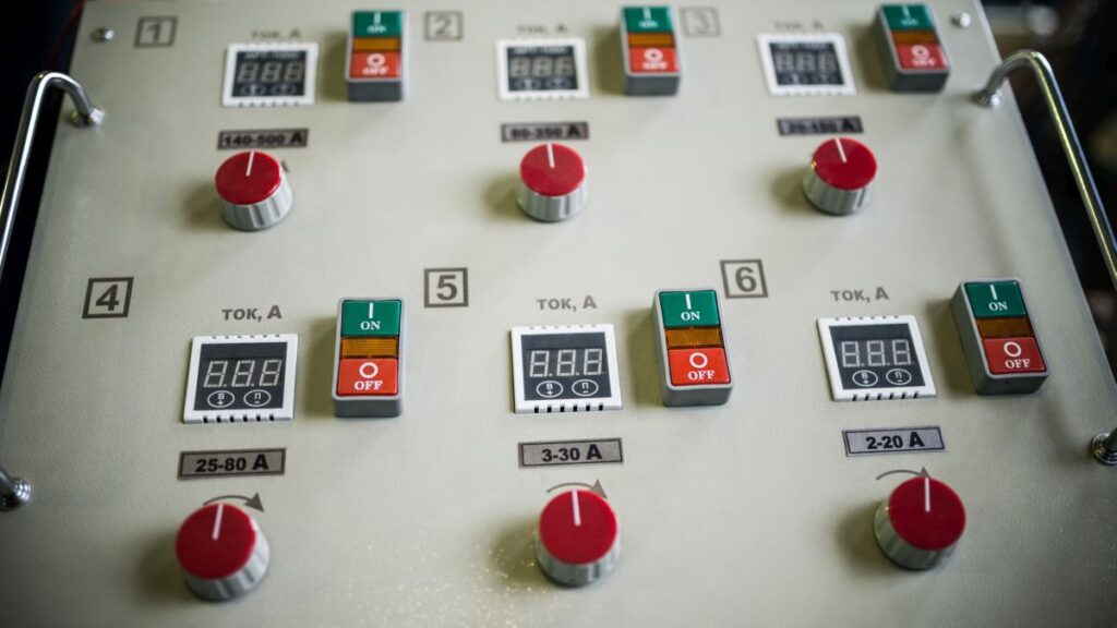 Electrical control panel with red dials digital amp displays and green and red switches for setting conductor current.