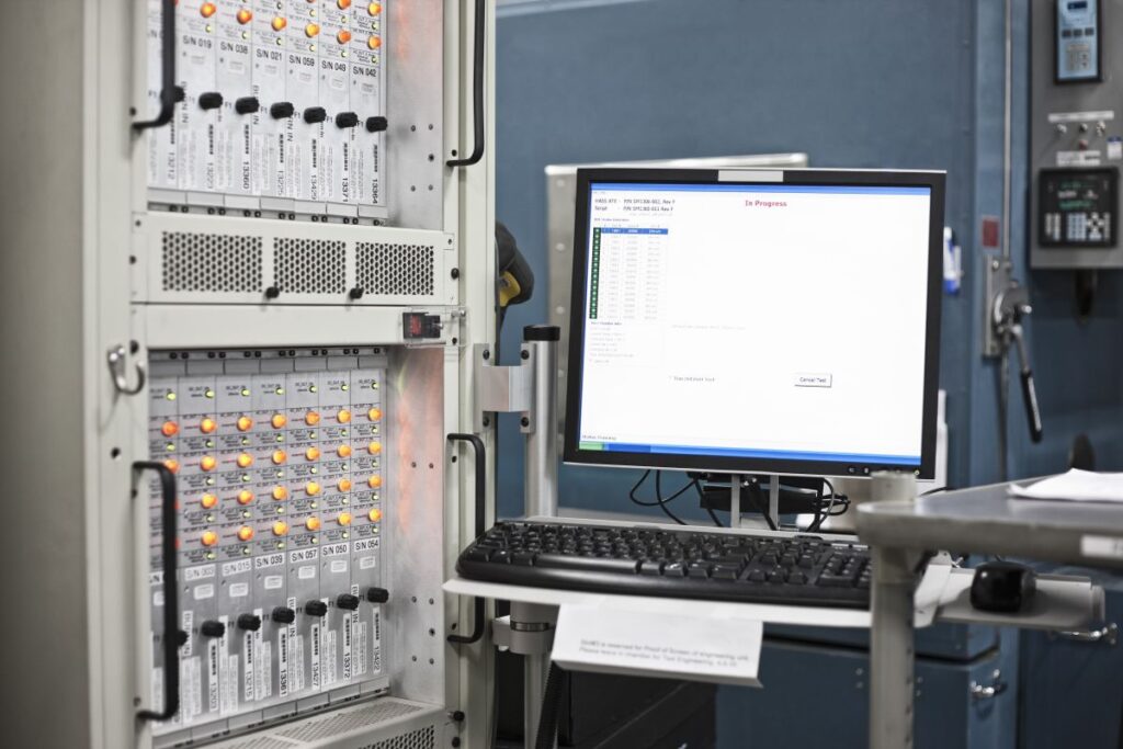 Computer workstation beside a rack of testing and control equipment in a research and development lab.