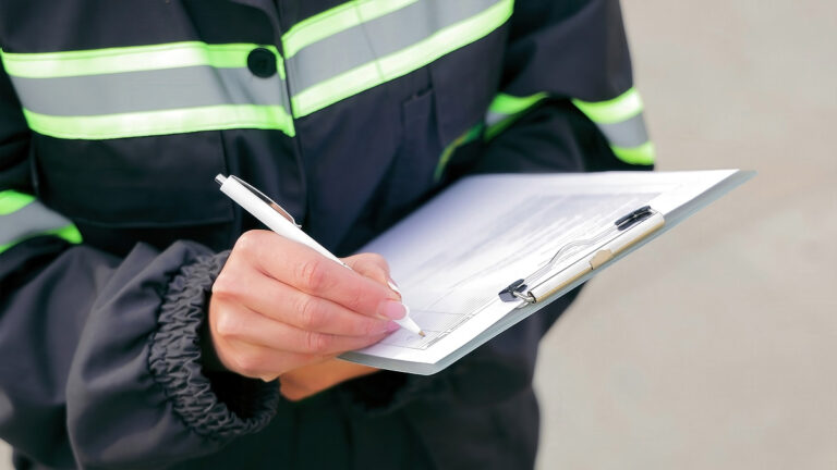 A worker in a reflective safety jacket fills out a clipboard during an emergency preparedness review.