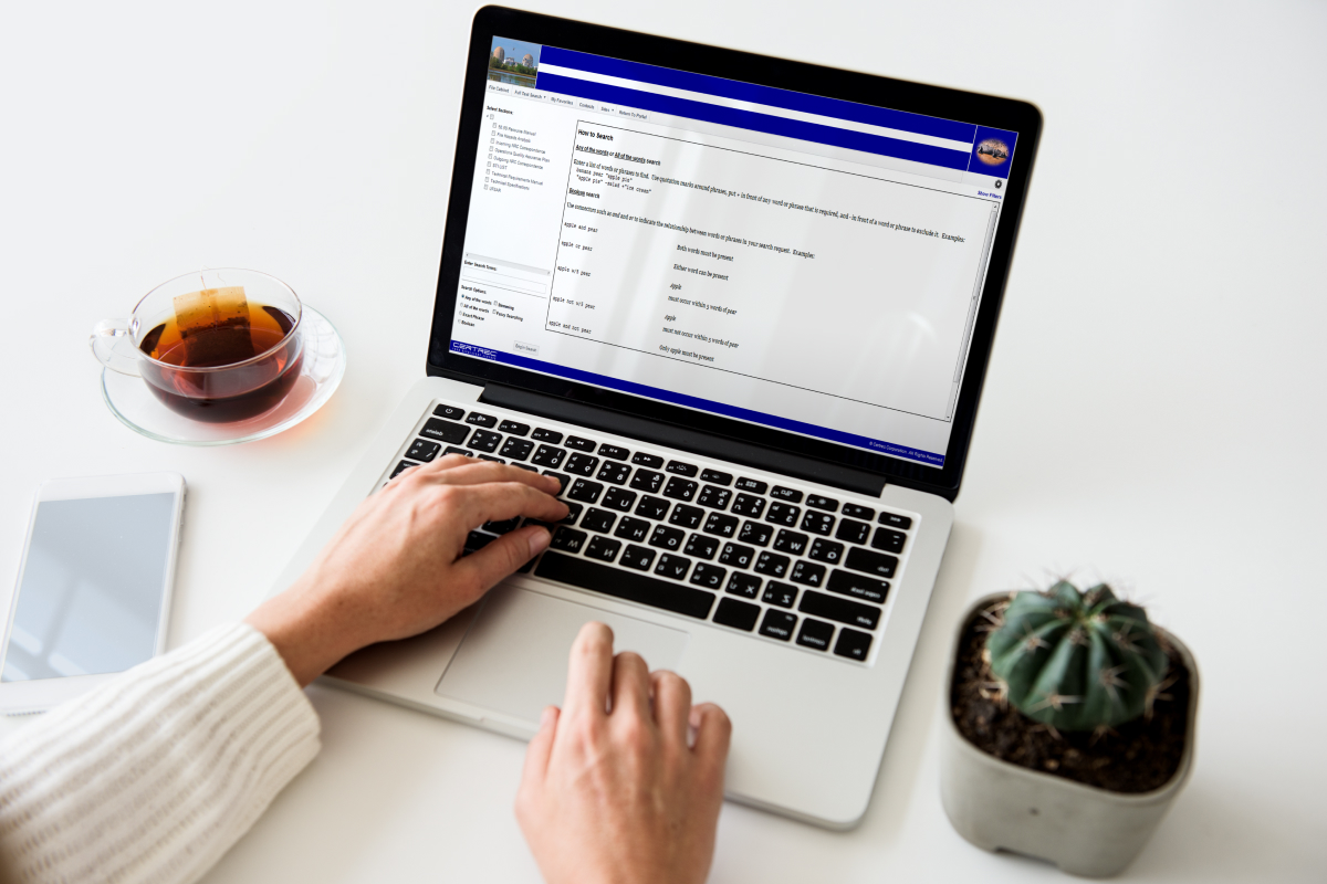 Person typing on a laptop with software dashboard open, next to a cup of tea and small plant on a desk.