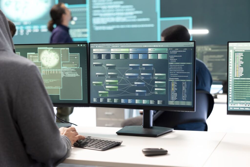 Person at a computer workstation monitoring cybersecurity dashboards on multiple screens in a modern office.