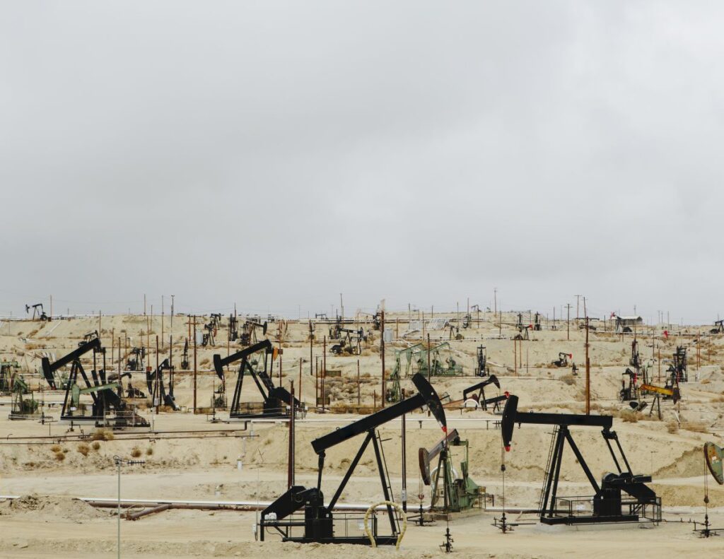 Desert oil field with multiple pumpjacks and wells spread across a dry landscape under a gray sky.