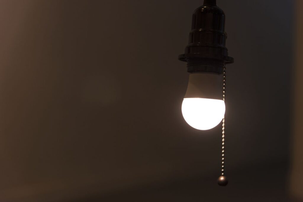 Bright light bulb hanging from a socket with a pull chain in a dark room.
