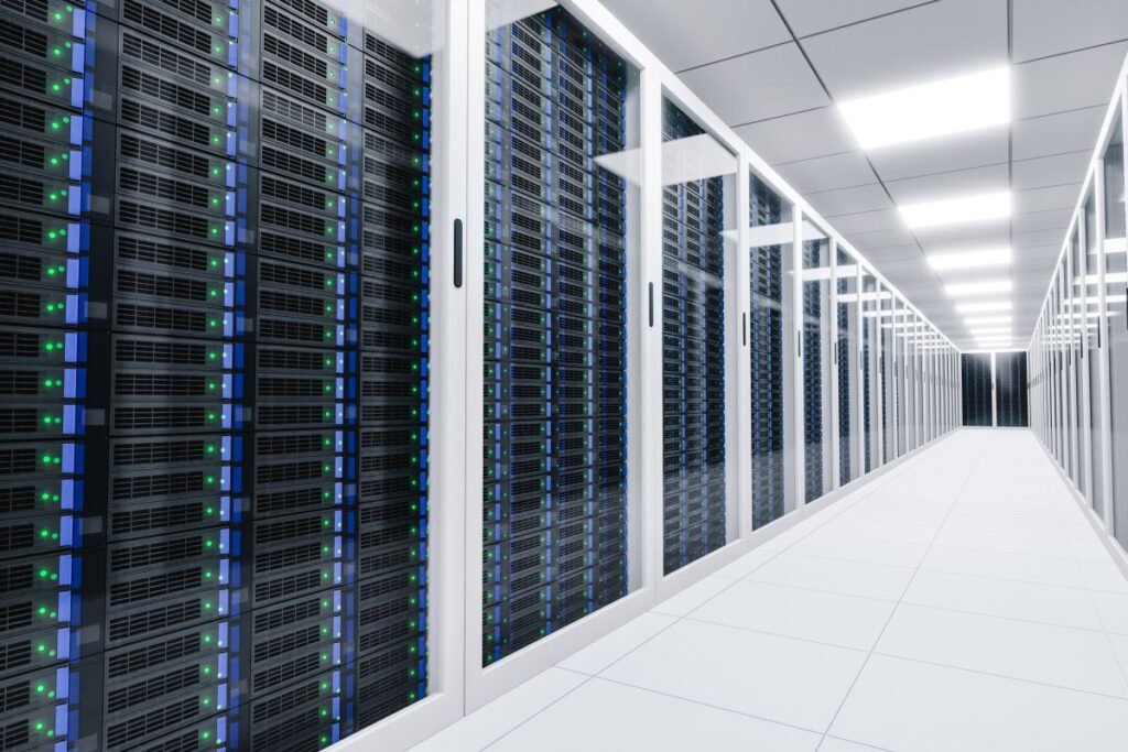 Long corridor inside a modern data center with rows of black server racks behind glass panels. Blue and green indicator lights line the servers, emphasizing high performance computing infrastructure in a clean, brightly lit environment.