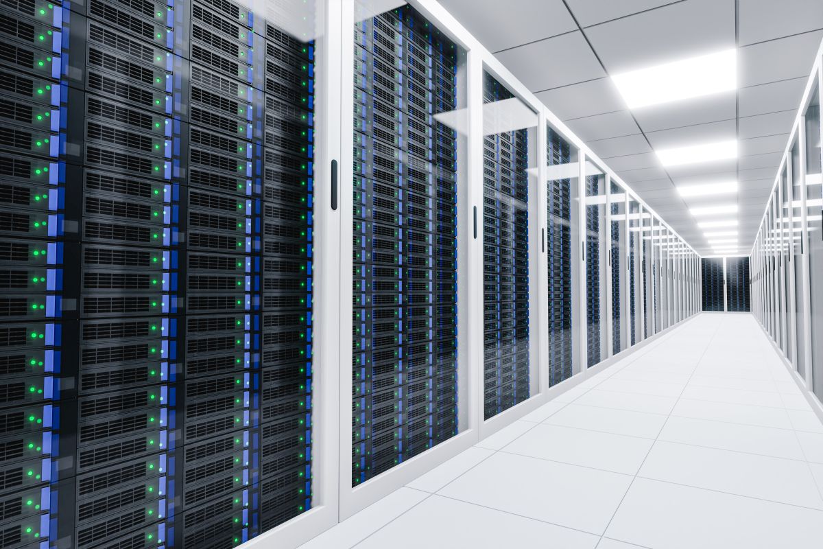 Long corridor inside a modern data center with rows of black server racks behind glass panels. Blue and green indicator lights line the servers, emphasizing high performance computing infrastructure in a clean, brightly lit environment.